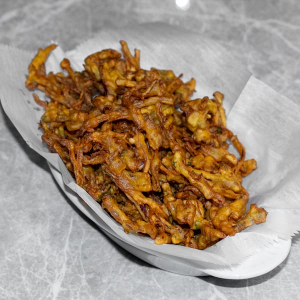 A white bowl filled with crispy, golden-brown Indian pakora, served on a grey marble table.