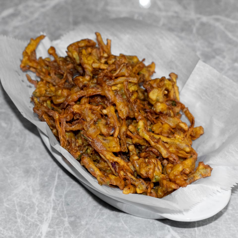 A white bowl filled with crispy, golden-brown Indian pakora, served on a grey marble table.