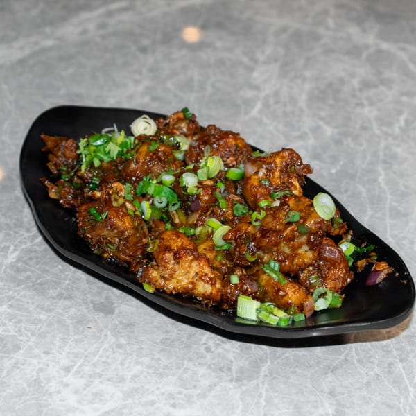 A black plate filled with Mitti Chulha's Indian chili chicken, garnished with green onions and cilantro.
