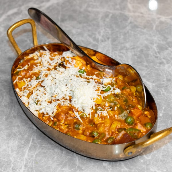 Indian vegetable curry with paneer cheese in a brass serving dish on a marble table.