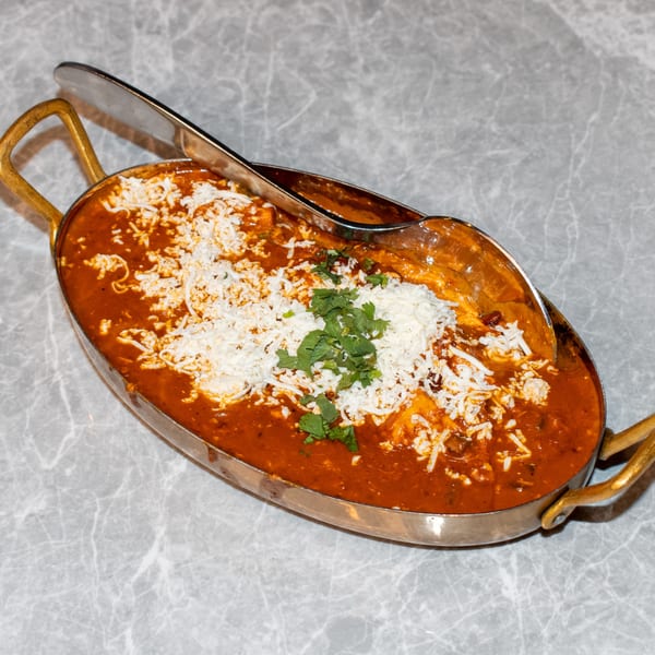 Indian curry with shredded cheese and cilantro in a brass serving dish with a spoon.