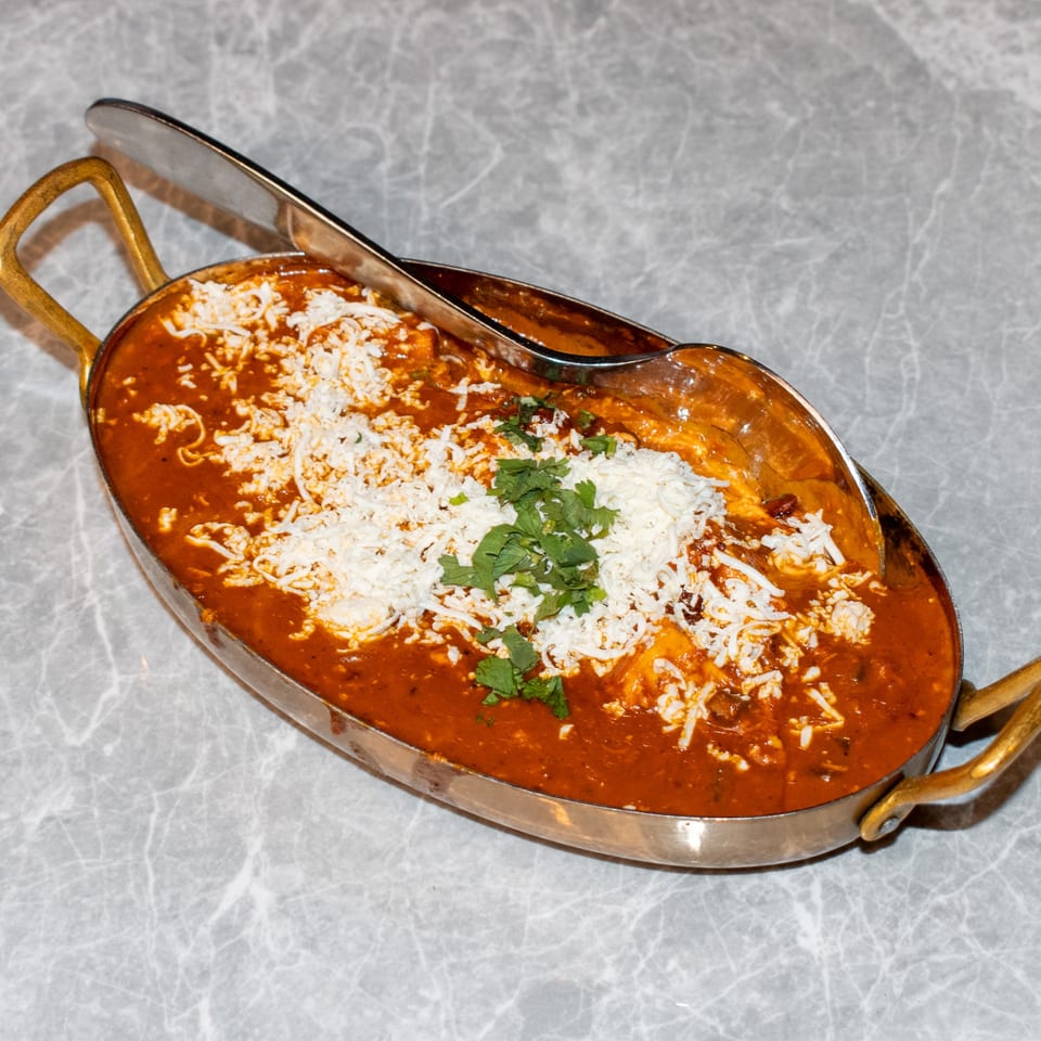 Indian curry with shredded cheese and cilantro in a brass serving dish with a spoon.