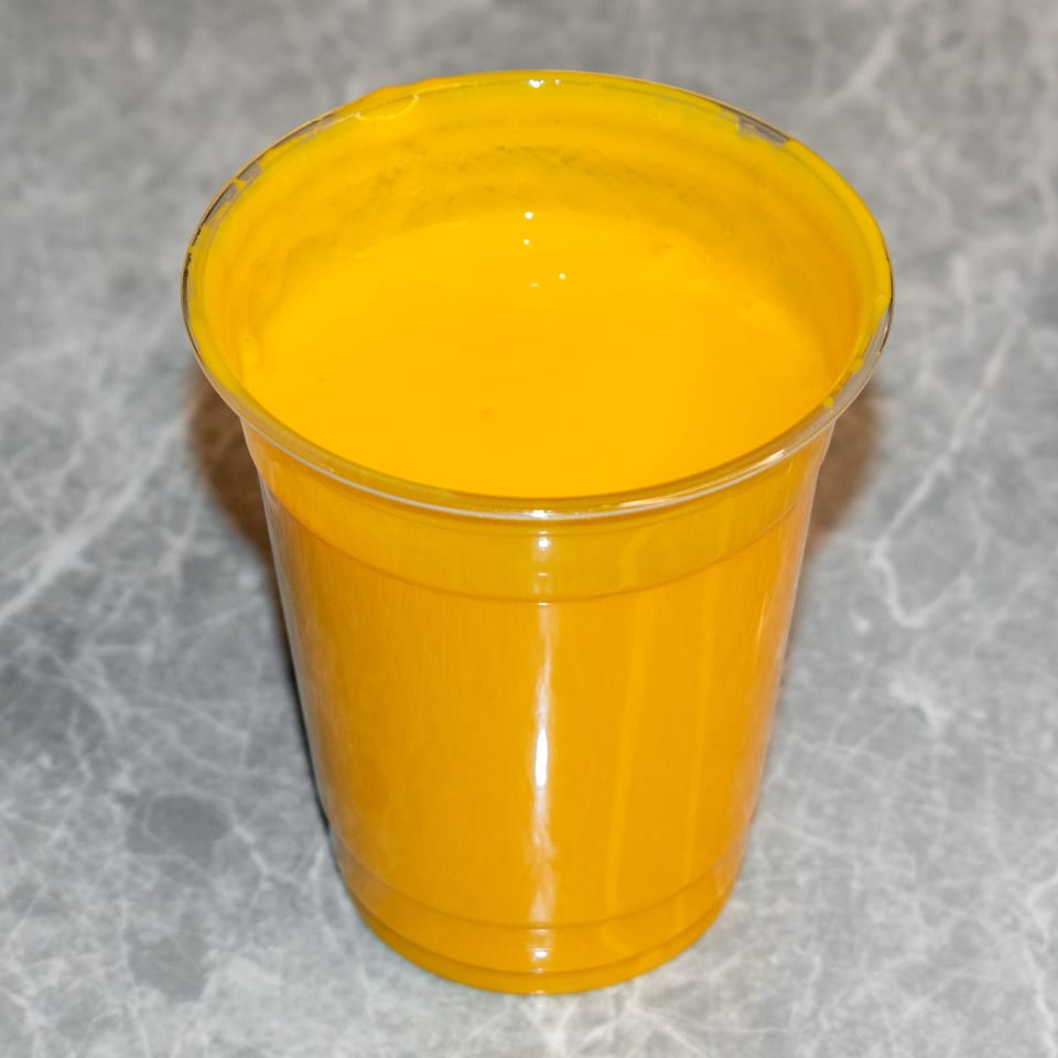 A vibrant yellow mango lassi in a clear plastic cup, sitting on a gray marble surface.