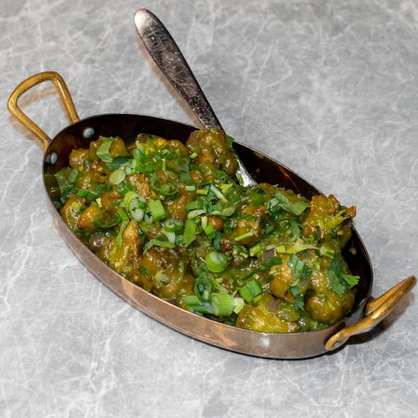 Mitti Chulha's green Indian curry, garnished with fresh herbs, in a brass serving dish with a spoon.