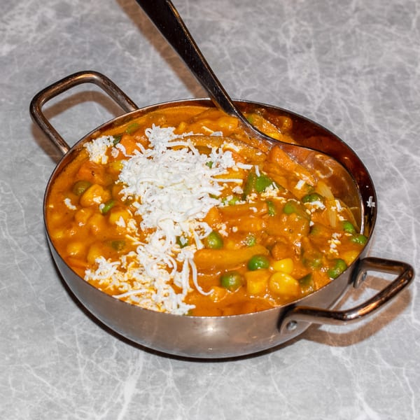 Indian curry with peas, potatoes, and shredded paneer in a metal serving dish with a spoon.