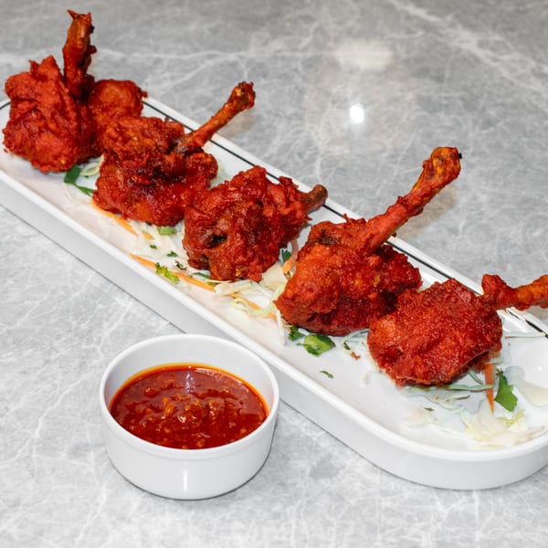 Five Mitti Chulha Indian Restaurant chicken lollipops with red sauce on a white platter.