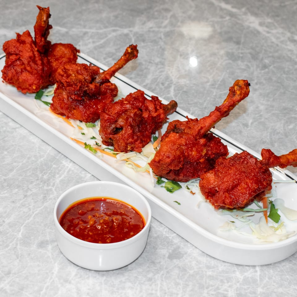Five Mitti Chulha Indian Restaurant chicken lollipops with red sauce on a white platter.