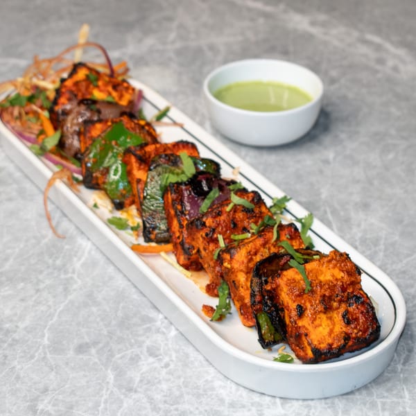 Indian paneer tikka with bell peppers and onions, garnished with cilantro, served with green chutney.